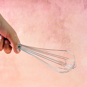 Hand holding a stainless steel hand whisk for mixing and blending ingredients