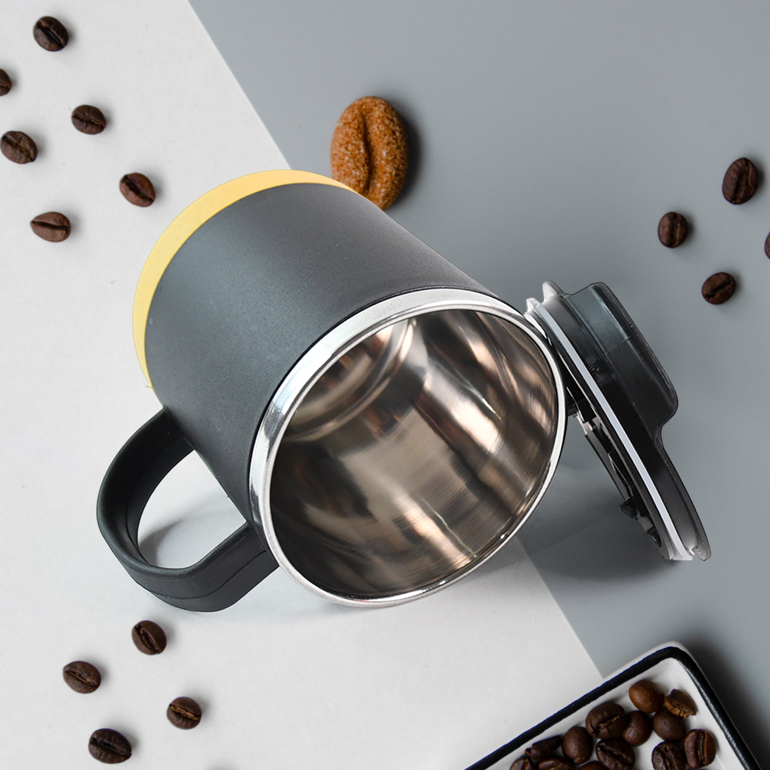 Superior eMart insulated coffee mug with black handle and yellow lid, surrounded by coffee beans