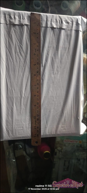 A brown wooden ruler measuring a white plastic mailing envelope. Markings show inches and centimeters.