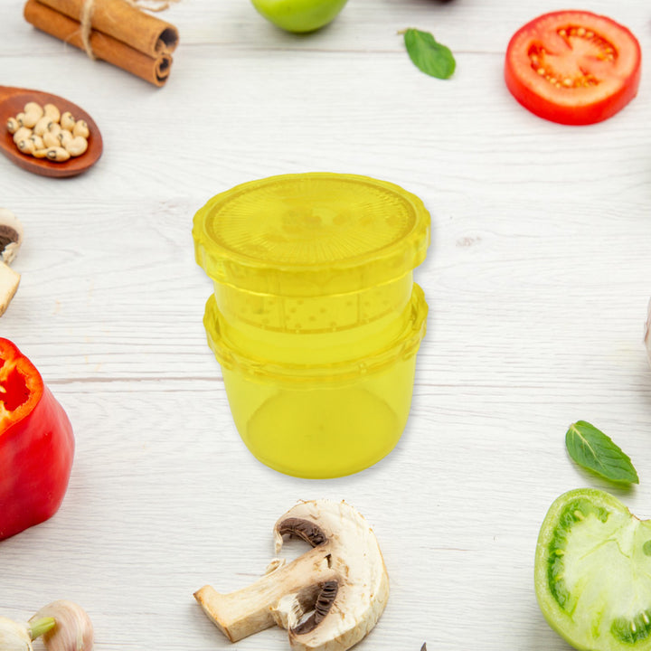 Manual citrus juicer and grinder in yellow surrounded by fresh vegetables and fruits on a wooden surface