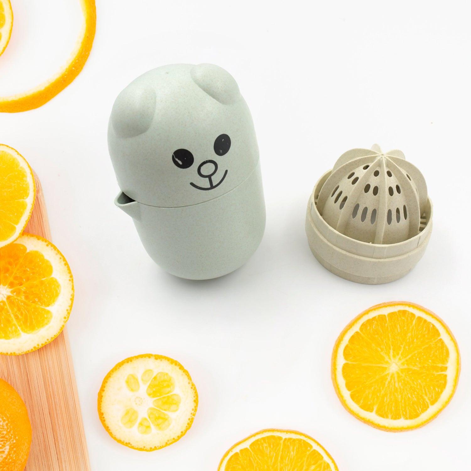 Cute green manual citrus juicer shaped like a bear with citrus slices on a wooden board