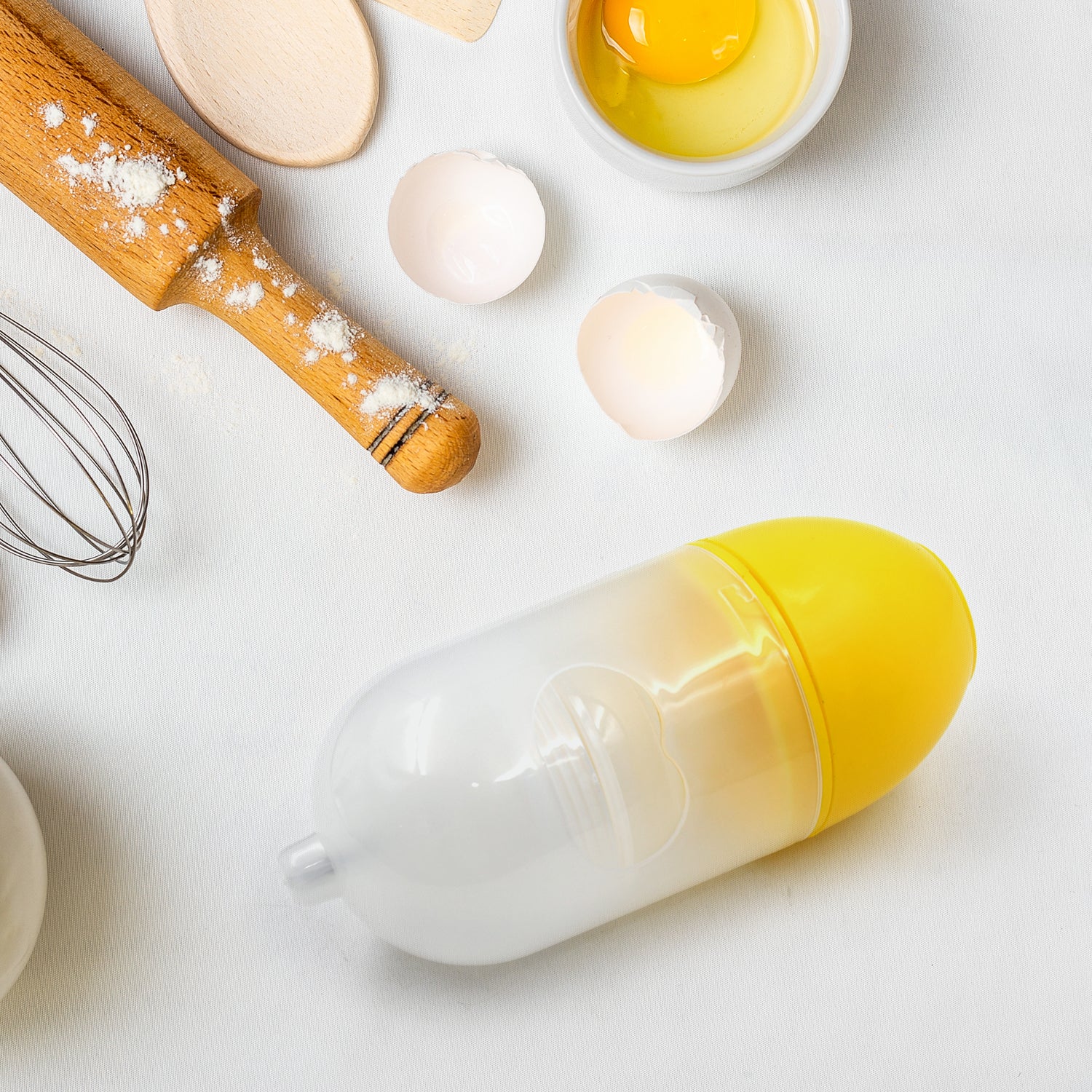 Manual egg scrambler with eggs, measuring spoons, and a whisk on a kitchen counter
