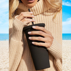 Matte studded tumbler with straw held by a person on a beach, perfect for summer hydration