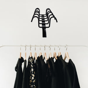 Black multi-purpose iron hanger hooks holding wooden hangers with black and floral clothes on white rack