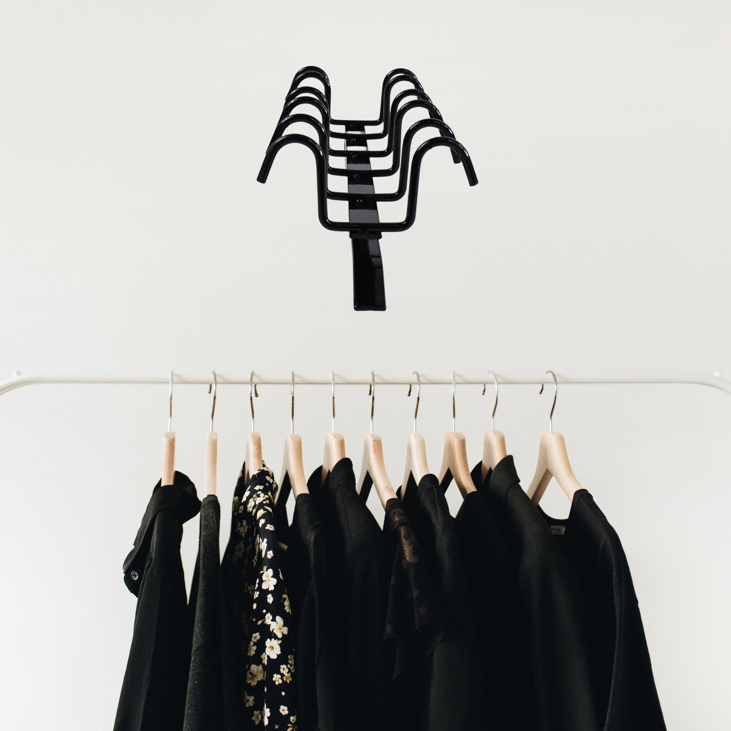 Black multi-purpose iron hanger hooks holding wooden hangers with black and floral clothes on white rack