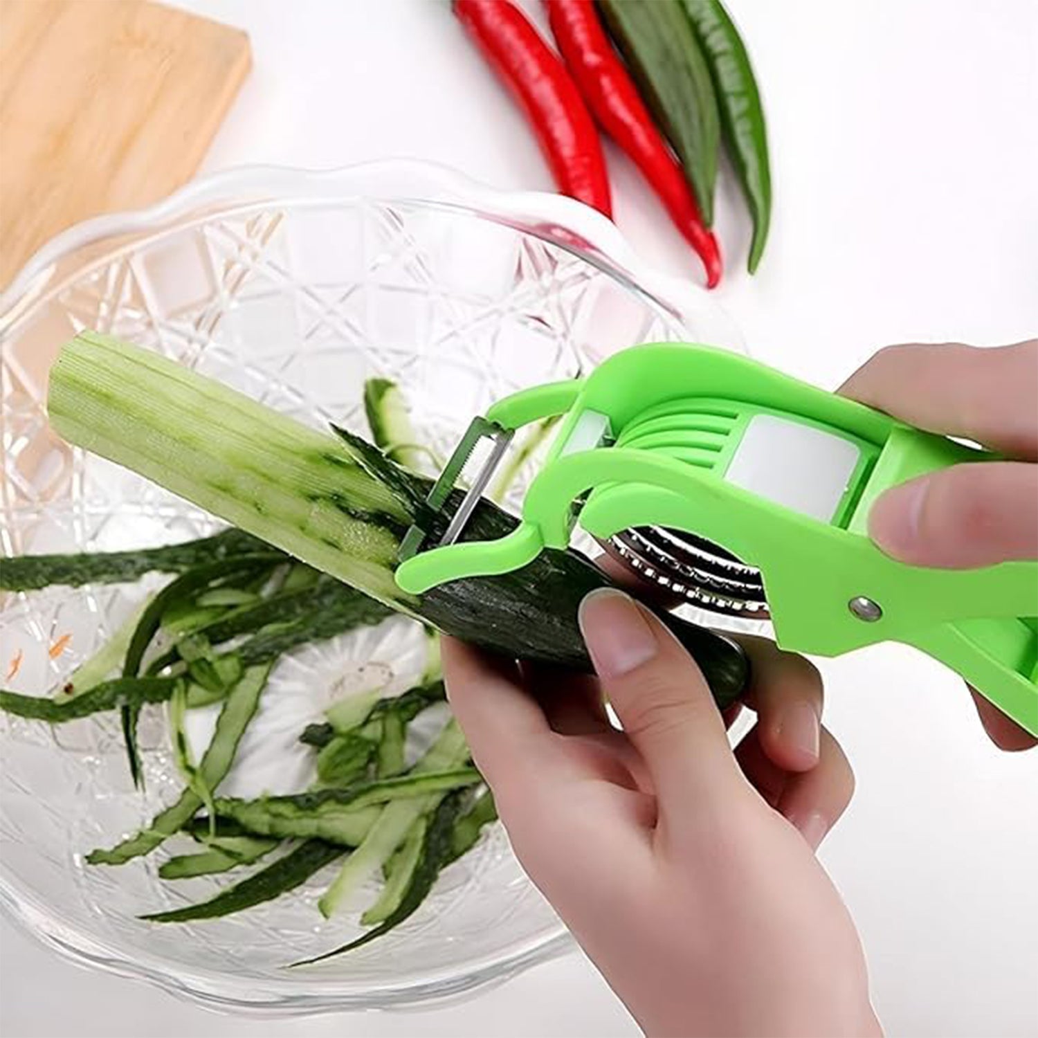 Superior eMart multi-purpose vegetable cutter peeling cucumber over glass bowl with red and green chili peppers nearby