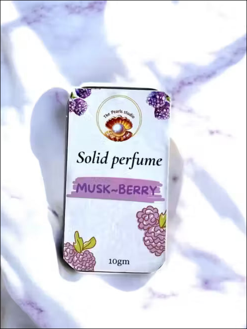 The Pearls Studio 10gm Musk-Berry solid perfume tin with berry illustrations, on a white marble background.