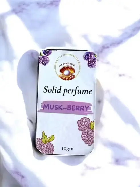 The Pearls Studio 10gm Musk-Berry solid perfume tin with berry illustrations, on a white marble background.