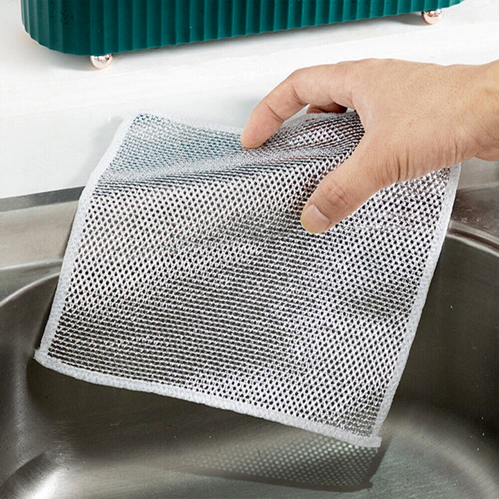 Hand holding a non-scratch stainless steel scrubber near a kitchen sink for effective cleaning