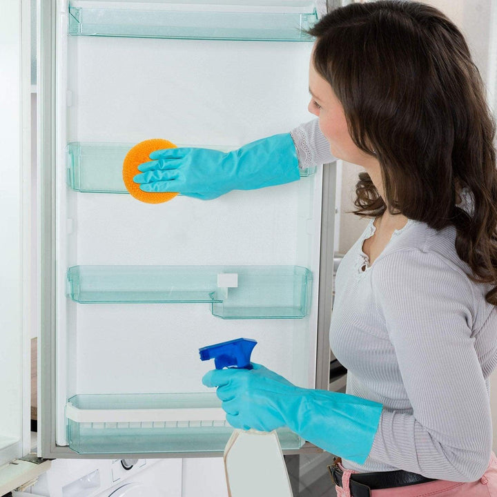 Woman using nylon scrubbers for dishes to clean a refrigerator with blue gloves