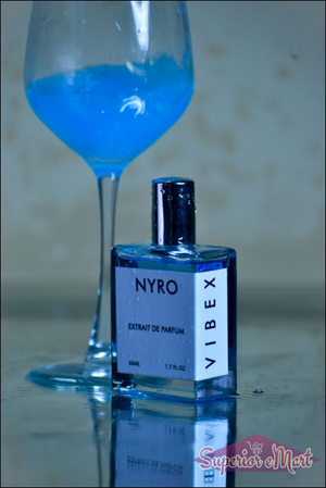 Nyro VIBEX Extrait de Parfum bottle next to a blue cocktail glass on a reflective surface