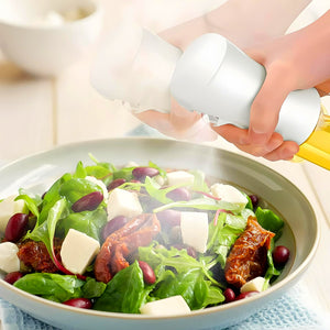 Oil spray bottle for cooking used to evenly mist fresh salad with olive oil and herbs