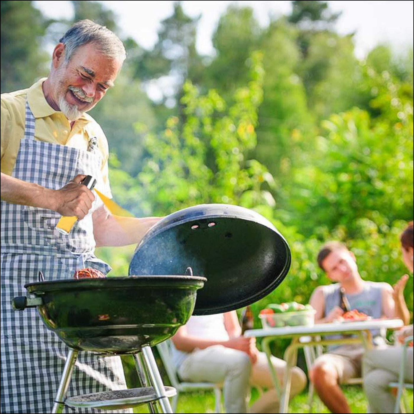 Man grilling outdoors using a glass oil sprayer for cooking, with friends enjoying nearby