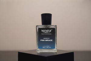 A rectangular glass perfume bottle with a black cap and a black-to-blue gradient label reading 'NEMAT SPRAY' and 'Inspired by Pink Mirage', displayed on a black pedestal against a warm beige background.