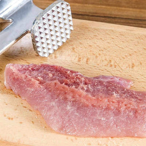 Professional meat tenderizer hammer resting on a wooden cutting board with raw meat