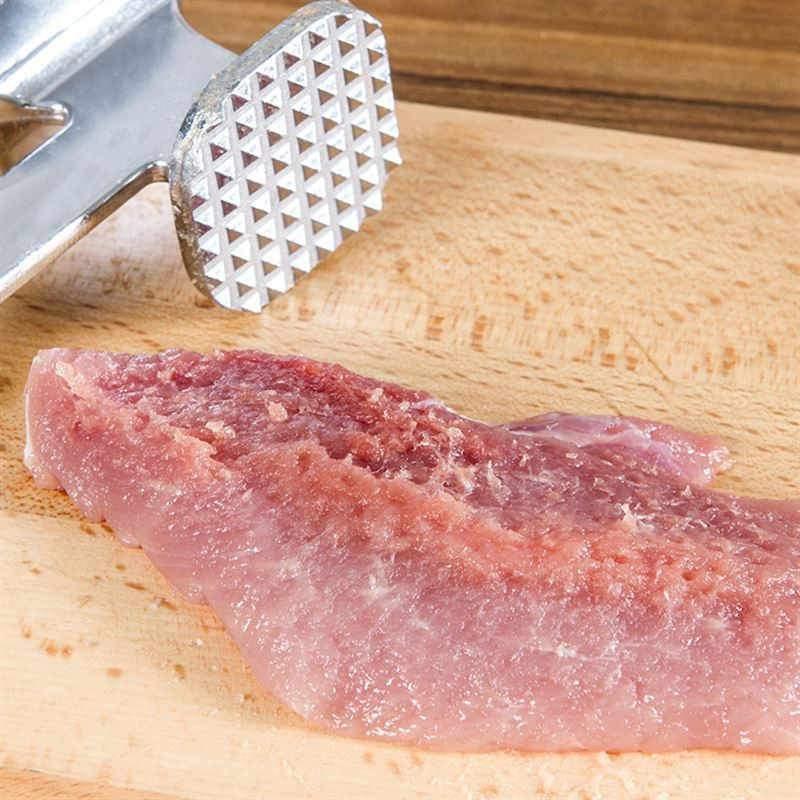 Professional meat tenderizer hammer resting on a wooden cutting board with raw meat