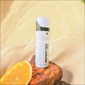 Reporter Midday Fragrance Spray 200ml on a wooden surface next to a fresh orange slice
