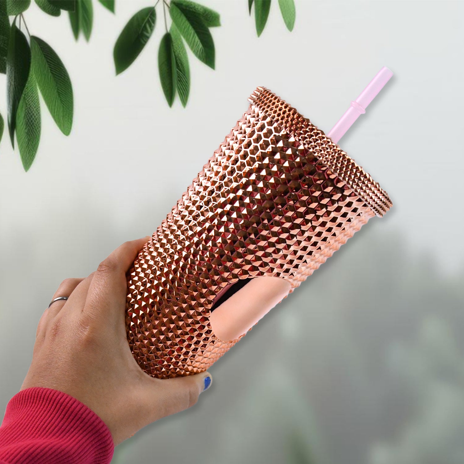 Hand holding rose gold studded tumbler with straw by Superior eMart against blurred background
