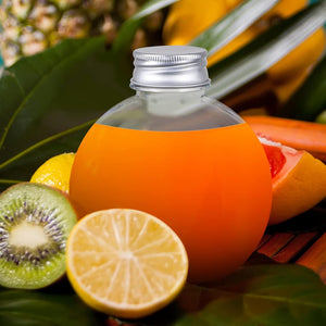 Round clear storage container filled with orange liquid surrounded by fresh fruit on green leaves