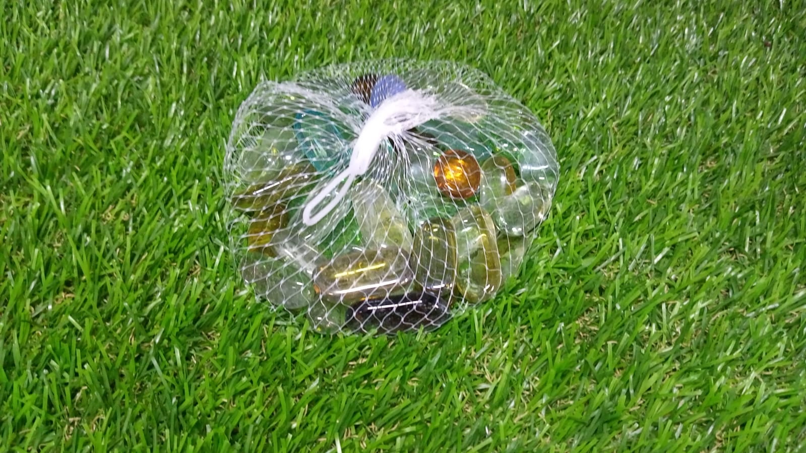 Bag of colorful round marbles for aquarium decoration on green grass