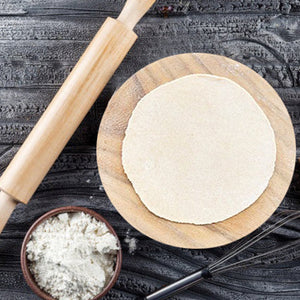 Round roti maker for home use with wooden rolling pin and fresh dough on a wooden board