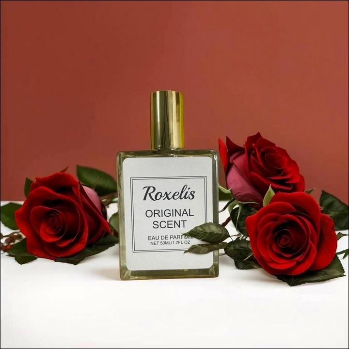 Roxelis Original perfume bottle surrounded by fresh red roses on a white surface