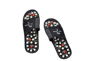 A pair of black Yoga Paduka acupressure slippers with white and red massage beads on the footbed, shown against a geometric gray and blue background with 'Yoga Paduka Acupressure' text and a 'PREMIUM QUALITY' badge.