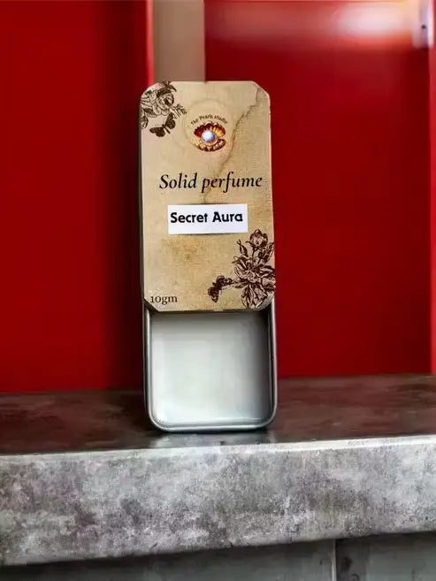 10gm Secret Aura solid perfume in a sliding metal tin with a vintage floral beige label and white balm.