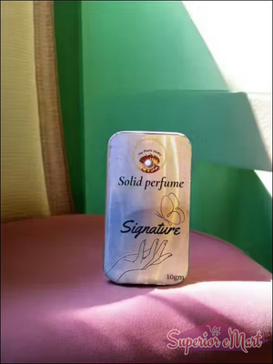 Solid perfume container labeled 'Signature' on a pink surface with a green background