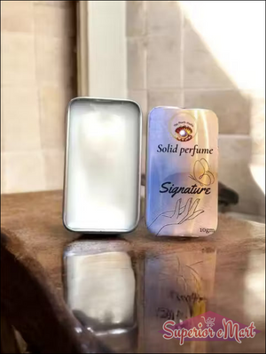 Two solid perfume containers on a reflective surface with a blurred background