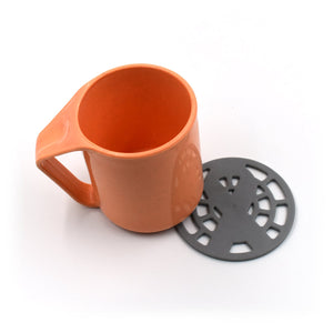 Silicone fancy coaster in gray beside an orange ceramic mug for home and kitchen use