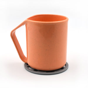 Silicone fancy coaster in grey supporting an orange measuring cup on a clean white background