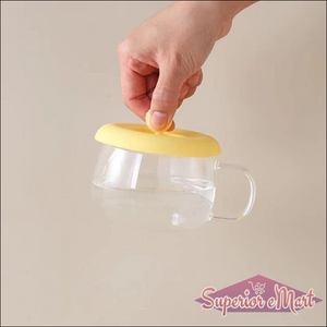 Silicone mug lid airtight seal in yellow being placed on a glass mug to preserve beverage freshness