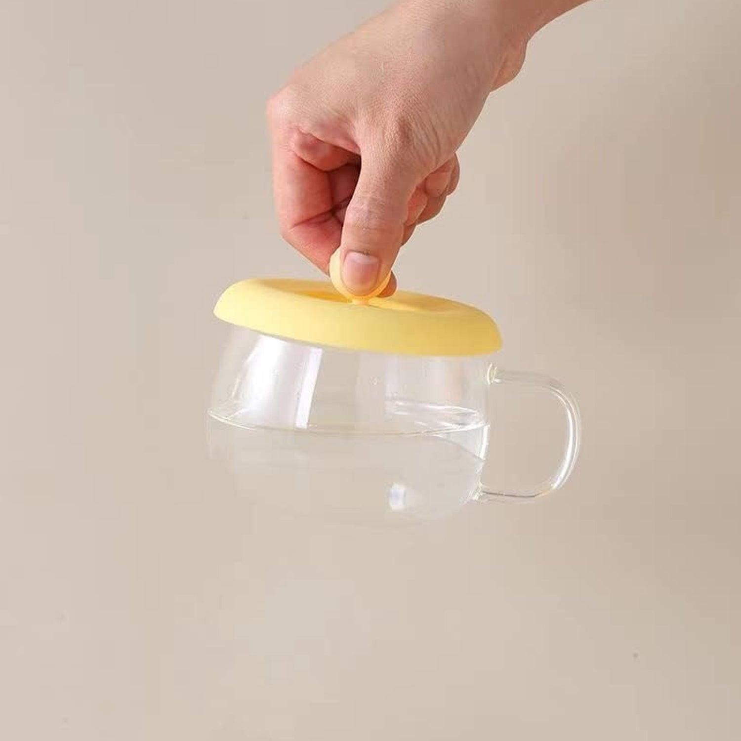 Silicone mug lid airtight seal in yellow being placed on a glass mug to preserve beverage freshness