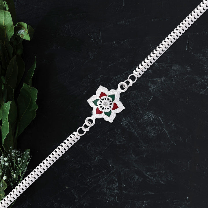 Silver plated rakhi bracelet with flower design and colored accents on a black background