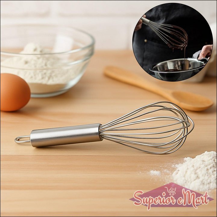 Small stainless steel balloon whisk on a wooden countertop with baking ingredients for easy mixing