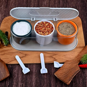 3 grid spice box with spoon, featuring containers for salt, chili flakes, and cumin on a wooden cutting board