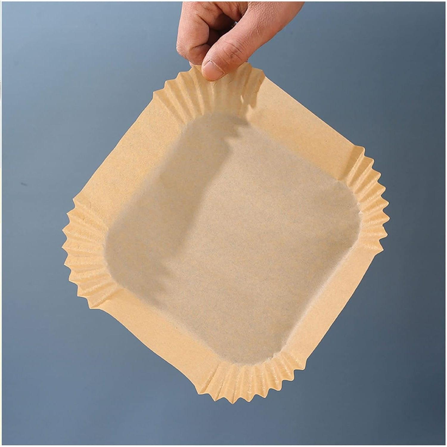 Hand holding a square air fryer liner disposable showcasing grease-resistant parchment material