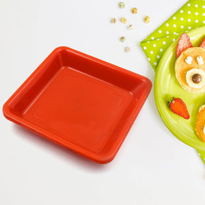 Bright red square dinner plate set on a green polka-dotted tablecloth with snacks