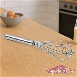 Superior eMart stainless steel hand whisk on a wooden kitchen countertop with eggs and milk in the background
