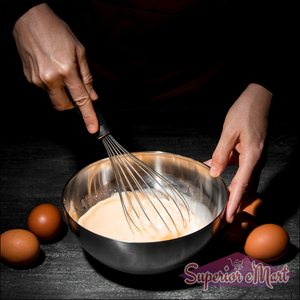 Stainless steel hand whisk being used to mix eggs in a bowl surrounded by eggs