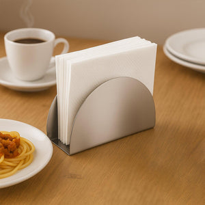Stylish stainless steel napkin holder with a modern design on a wooden table beside a coffee cup
