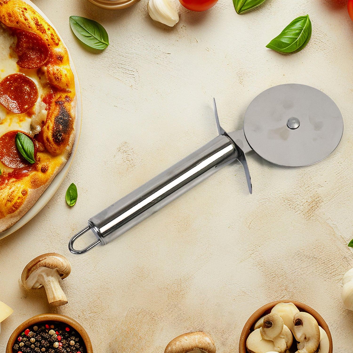 Stainless steel pizza cutter on a wooden table with fresh pizza and ingredients around it