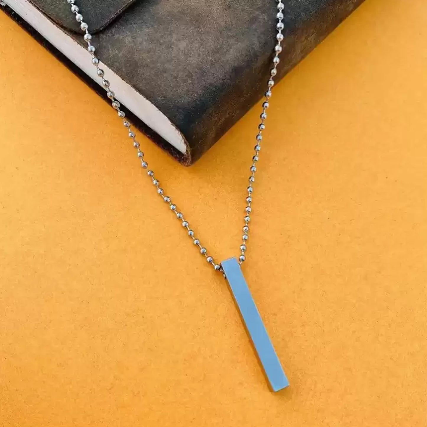 Stainless steel stick necklace on a brown and orange background, perfect for everyday wear