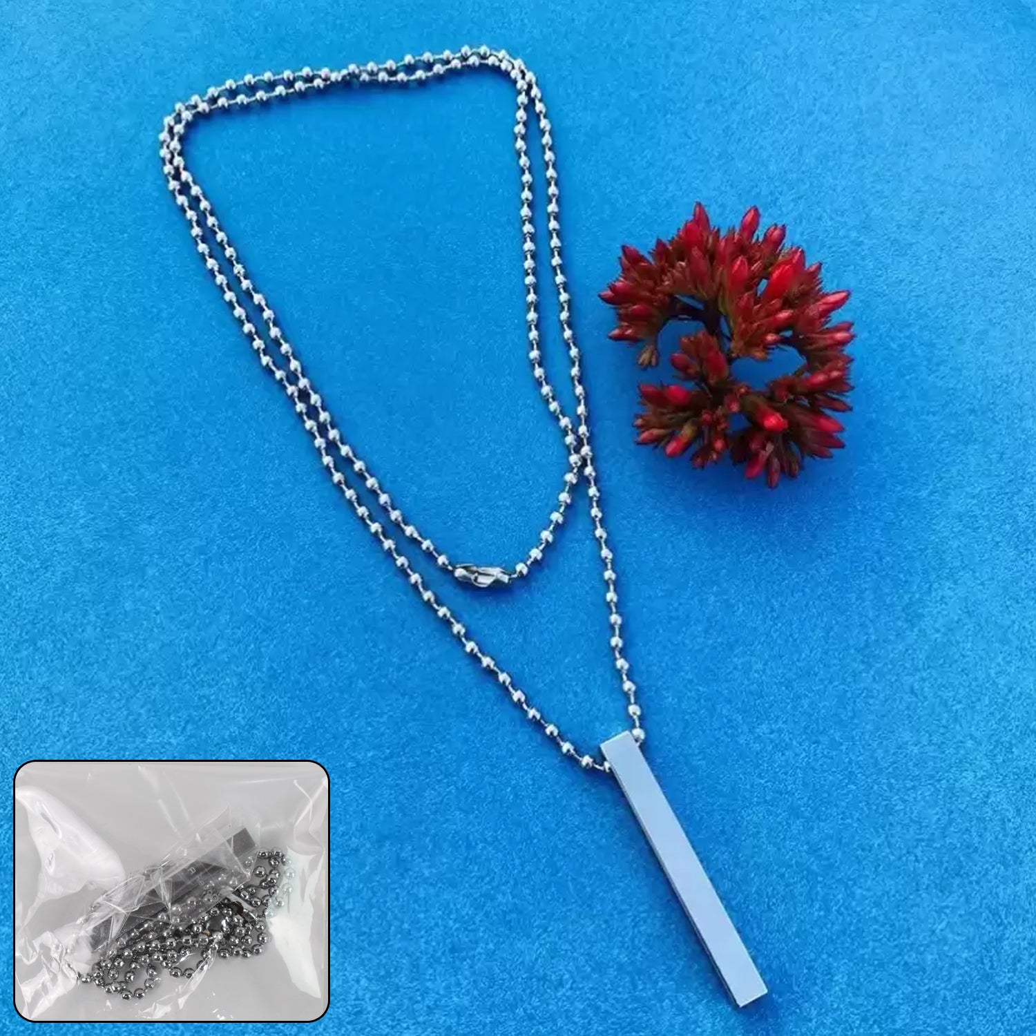 Stainless steel stick necklace with a sleek design hanging on a blue surface beside a red flower