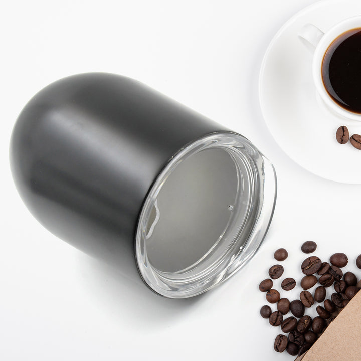 Sleek black stainless steel travel mug next to a cup of coffee and coffee beans