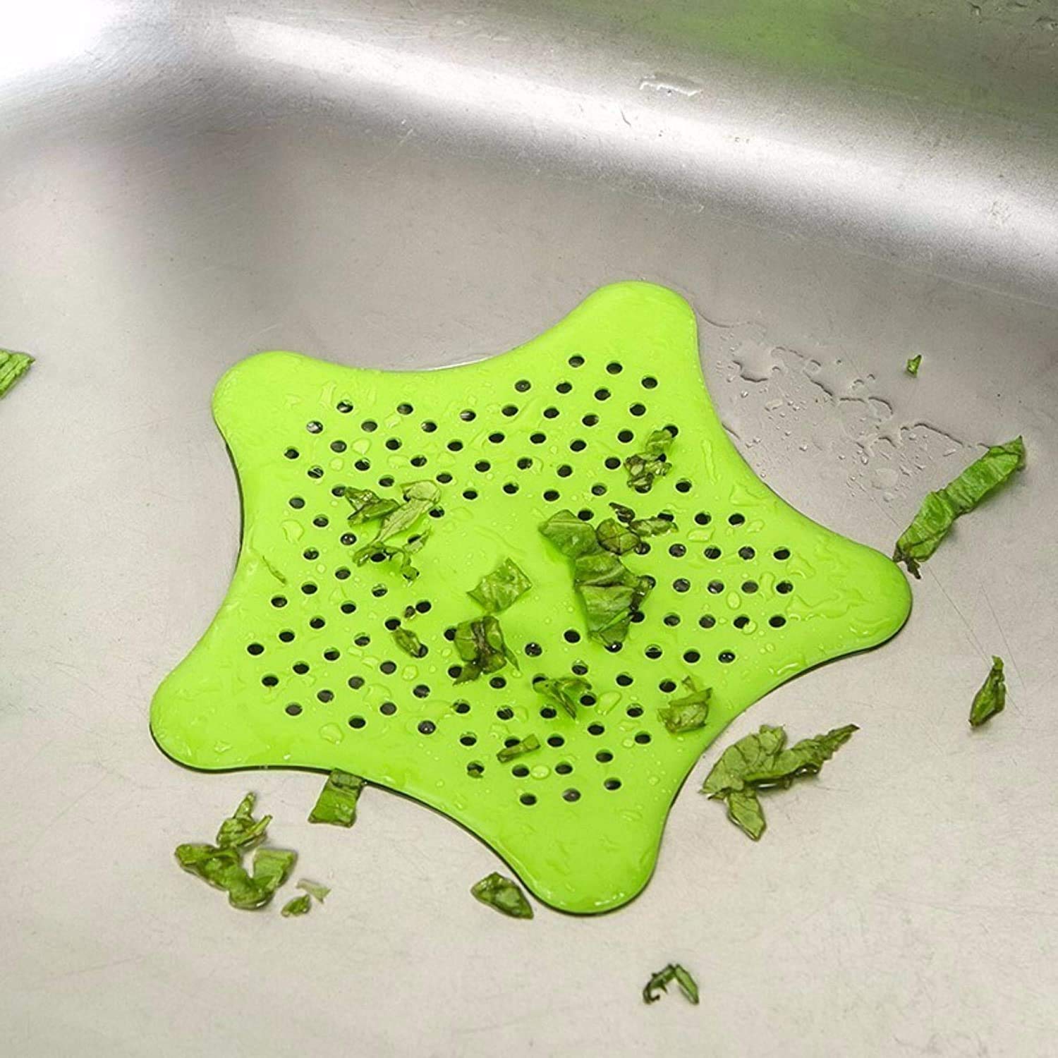Green star shape sink strainer with drainage holes collecting food scraps in a kitchen sink
