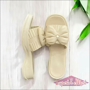Beige platform slide sandals featuring a large decorative bow and pleated strap design.