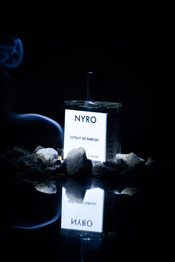 Nyro Extrait de Parfum with Dark Edge in a sleek bottle surrounded by stones and smoke