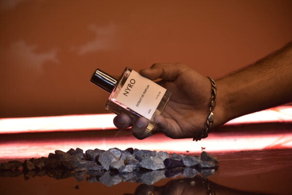 Nyro perfume bottle held above dark stones, showcasing the scent Dark Edge with a bold design